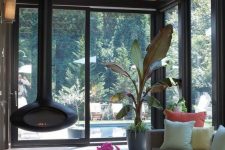a stylish modern sunroom with a grey sofa, a low coffee table, a black suspended fireplace and potted plants