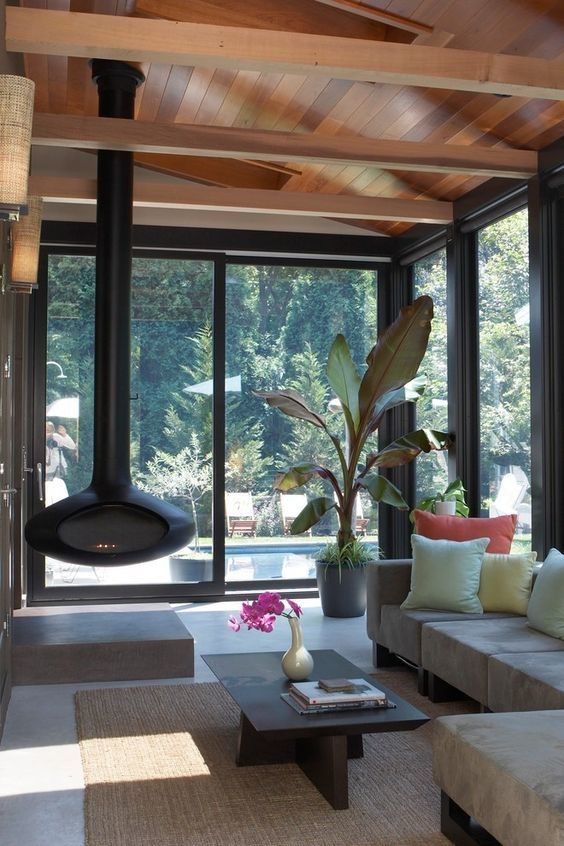 a stylish modern sunroom with a grey sofa, a low coffee table, a black suspended fireplace and potted plants