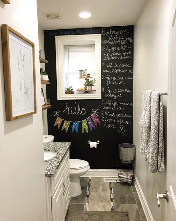 a tiny powder room with a chalkboard accent wall, a white vanity with a sink, a mirror with shutters, some decor and greenery