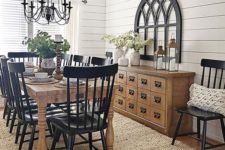 a traditional farmhouse dining space with black chairs, a light stained buffet and table, a metal chandelier