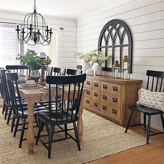 a traditional farmhouse dining space with black chairs, a light stained buffet and table, a metal chandelier