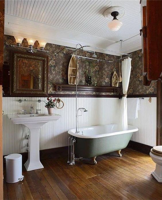 a vintage farmhouse bathroom with a wooden floor, white beadboard, moory wallpaper and vintage fixtures
