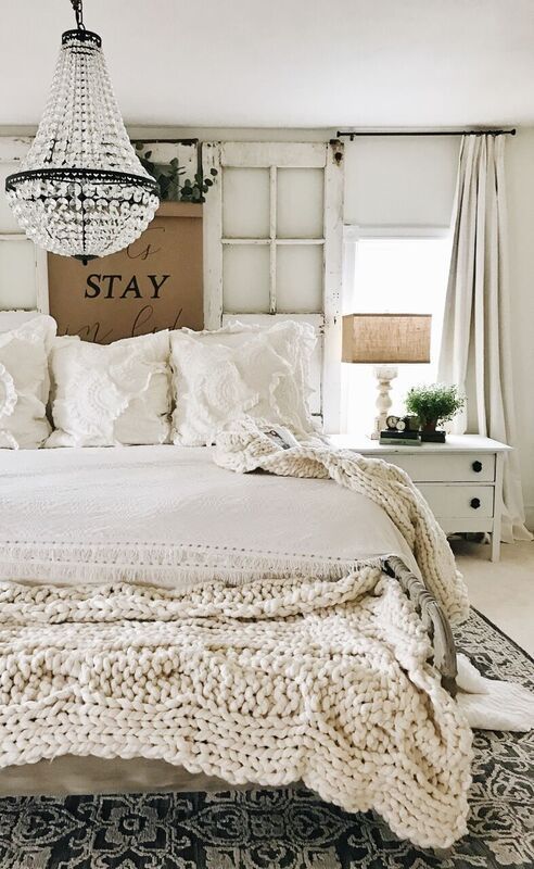 a vintage farmhouse bedroom with vintage doors as a headboard, lace and knit textiles and a refined crystal chandelier