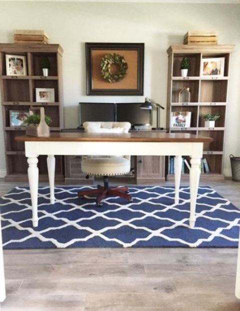 a vintage farmhouse home office with white walls, open storage units, a vintage desk, a blue printed rug, a leather chair and some art