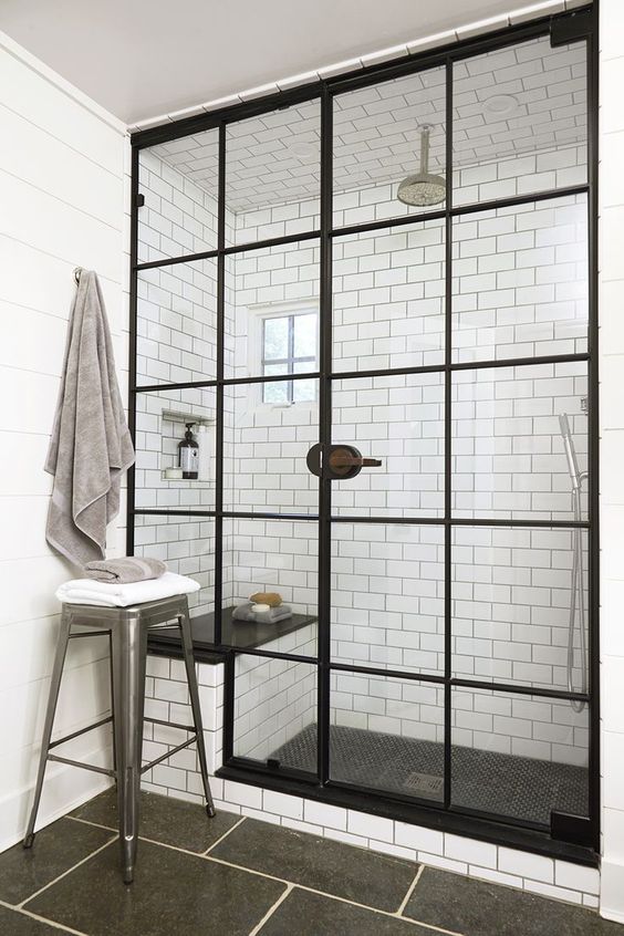 a vintage-inspired bathroom with white subway and graphite grey tiles, a shower space with black frame doors and a bench inside