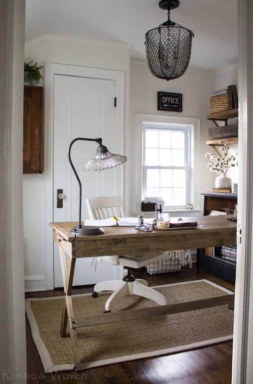 a welcoming farmhouse home office with a wooden desk, a jute rug, open shelves, a metal chandelier and a crystal lamp