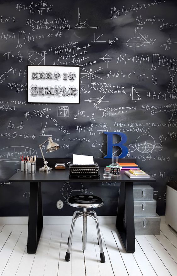 a welcoming home office with a chalkboard accent wall, a black desk, a metal stool, a metallic lamp and some metal boxes for storage