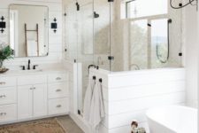 a white farmhouse bathroom with plank walls, grey hex tiles, an oval tub, a vintage vanity and touches of black