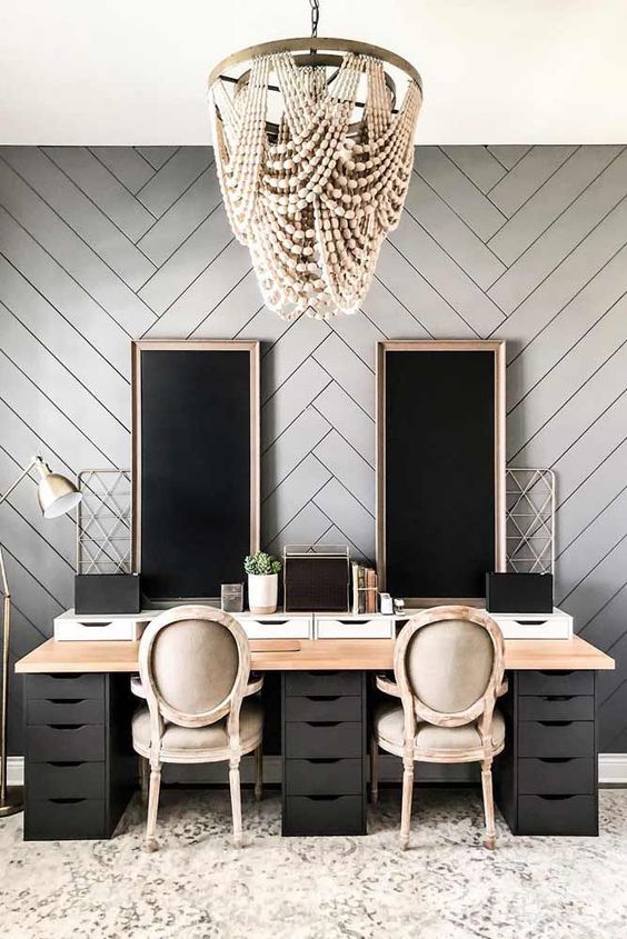 an elegant vintage farmhouse home office with a grey chevron accent wall, a shared black desk, neutral chairs and chalkboards