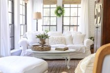 an elegant vintage farmhouse sunroom with white furniture, a chalk painted table, greenery and shades
