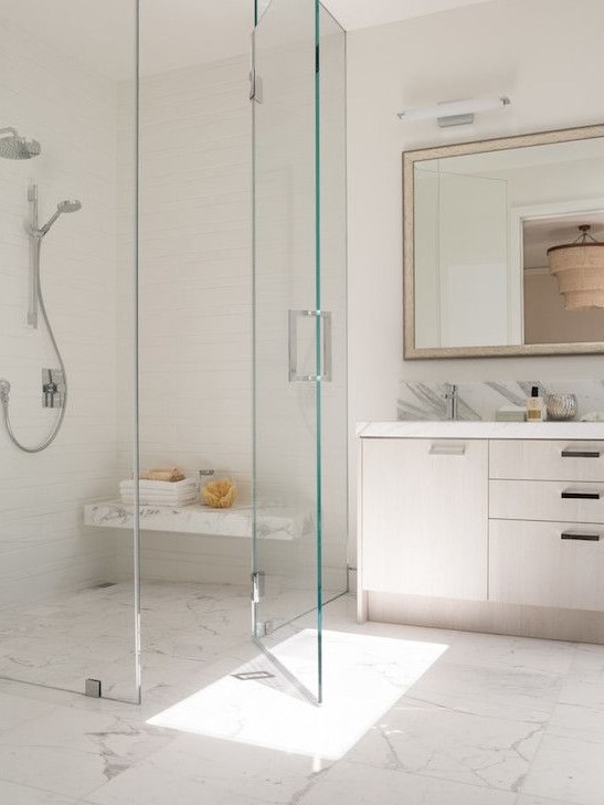 an ethereal shower space with a marble tile floor and a floating bench that matches plus seamless glass doors