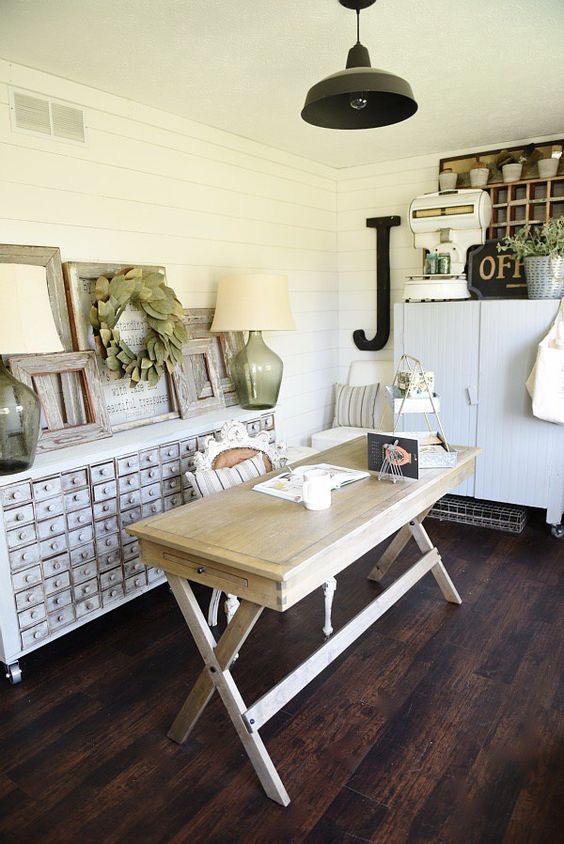 an inspiring home office with white beadboard walls, a wooden desk, a shabby chic storage unit, a black lamp and some decor