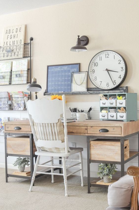 an inviting farmhouse home office with a wood and metal desk, a white chair, storage units and a large clock