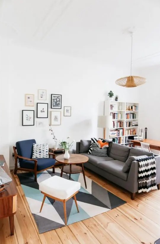 a Scandi living room with a geo printed rug, a navy chair and a white pouf, a wooden coffee table, a gallery wlal and a grey sofa with printed textiles