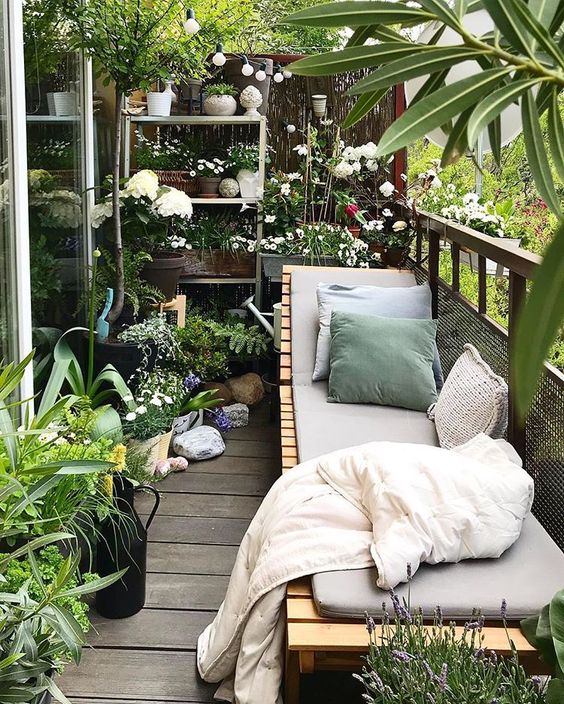 a balcony garden with potted greenery and blooms and a wooden lounger with upholstery and pillows is a gorgeous place to be