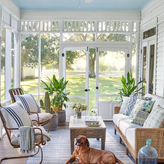 a beachy sunroom with rattan furniture, printed textiles, a wooden table and some potted plants