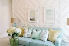 a beautiful coastal living room with a white geometric pattern wall, a blue sofa, white furniture, artworks and white blooms