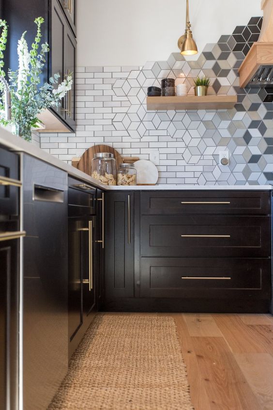 a black kitchen with shaker style cabinets, white stone countertops, a subway and geo tile backsplash, wooden shelves and a brass pendant lamp