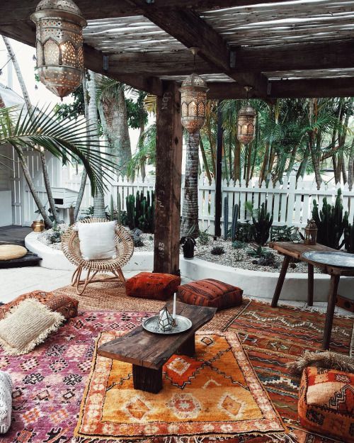 a boho terrace with colorful layered rugs, bright cushions and pillows, a rattan chair, Moroccan lanterns and cacti all around