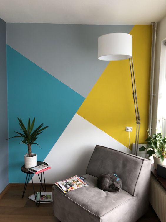 a bold and cool nook with a geometric color block accent wall, a grey chair, a floor lamp, potted greenery and a side table