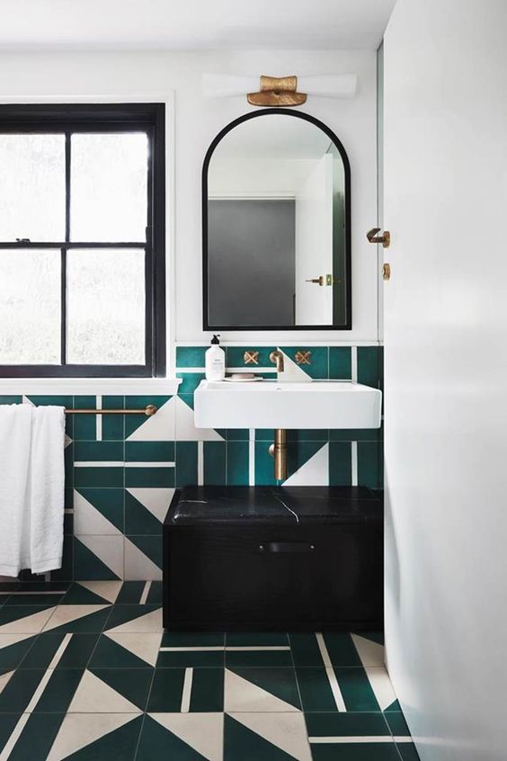 a bold art deco bathroom with green and white geo tiles, white appliances and a black vanity plus brass fixtures here and there