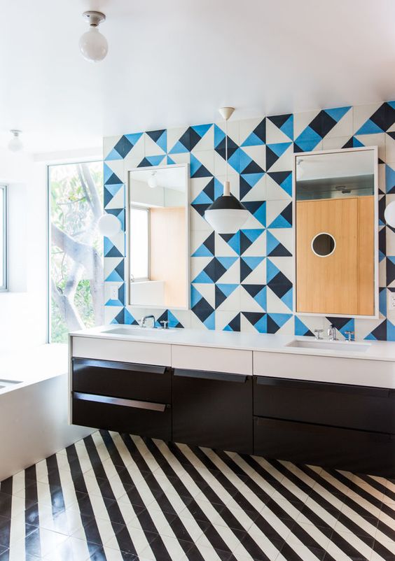 a bold bathroom with a striped black and white tile floor, a black vanity, white appliances, a blue, black and white tile wall