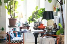a bold book with potted plants and trees, a round table and chairs, a bold floral rug and some vintage decor