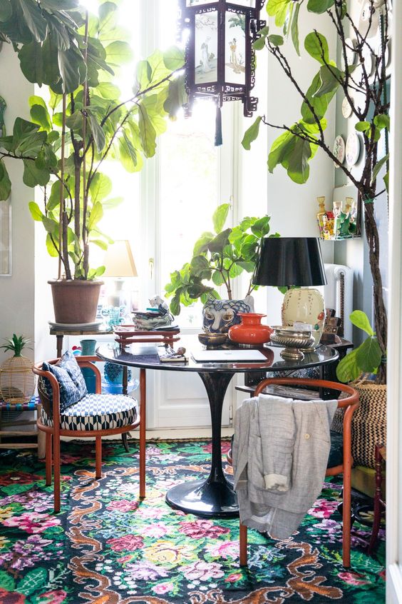 a bold book with potted plants and trees, a round table and chairs, a bold floral rug and some vintage decor