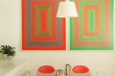 a bold dining space with red, orange and green geometric artwork, a glass dining table and red curved dining chairs plus a pendant lamp