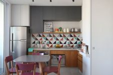 a bold kitchen with graphite grey and stained cabinets, a colorful geo tile backsplash, a table and fuchsia chairs is a lovely space