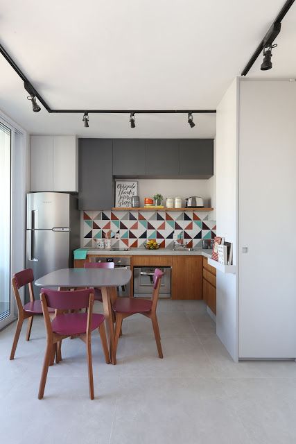 a bold kitchen with graphite grey and stained cabinets, a colorful geo tile backsplash, a table and fuchsia chairs is a lovely space