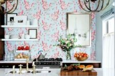 a bright and catchy space with only lower cabinets, with bright floral wallpaper, open shelving,a kitchen island with seating and large chandeliers