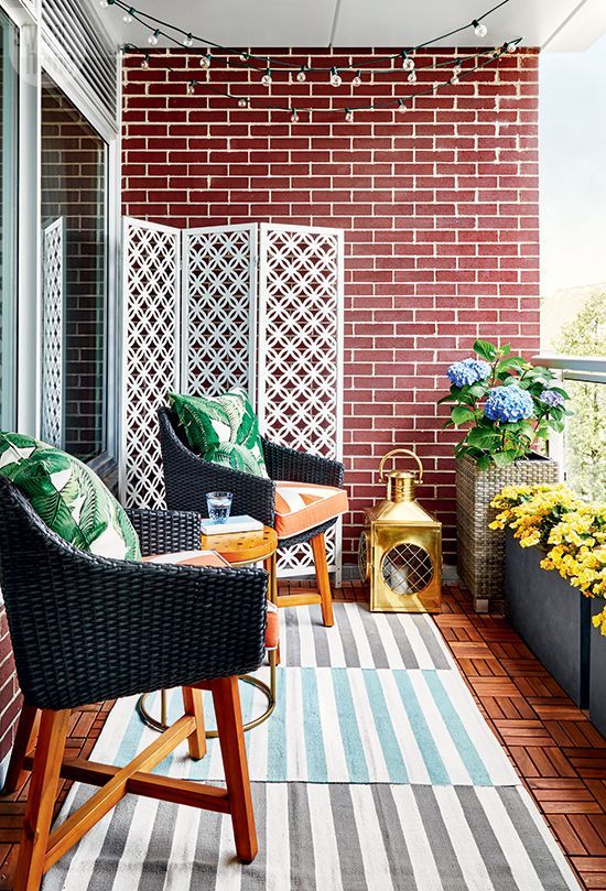 a bright and stylish balcony with layered rugs, wicker chairs and printed pillows, potted blooms and a large candle lantern