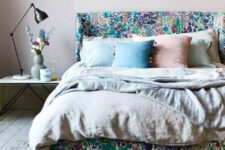 a bright bedroom with a bold upholstered bed and pastel bedding, a floral rug, a nightstand with a black table lamp