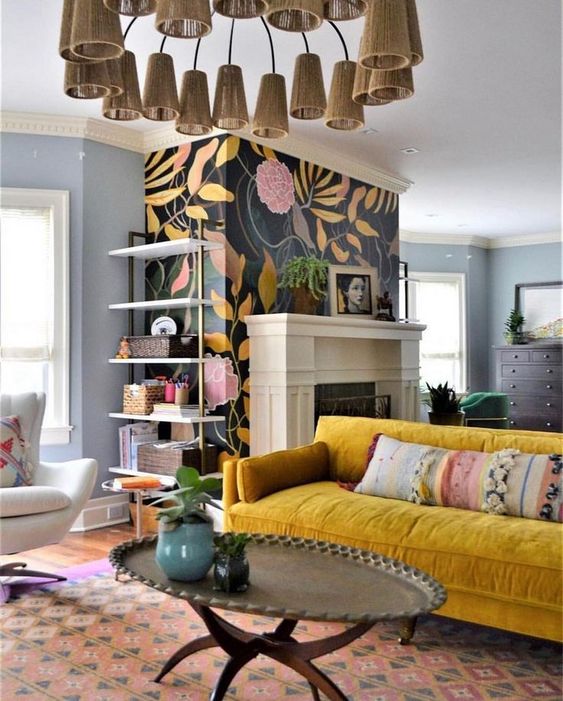 a bright living room with a black floral accent wall and a fireplace, a mustard sofa, chairs and coffee tables