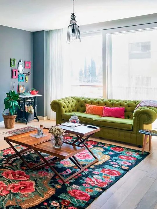 a bright living room with a console table and a colorful frame gallery wall, a green sofa, a bright floral rug and coffee tables