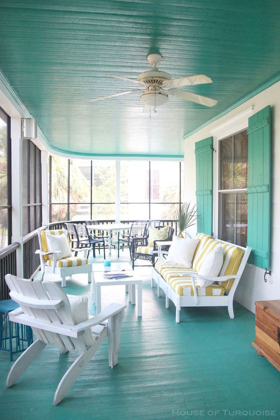 a bright mint blue sunroom with white wooden furniture, striped upholstery and a cozy dining space