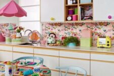 a bright retro kitchen with white flat panel cabinets, a bright pink wallpaper backsplash, a bright pink pendant lamp and pastel blue dining furniture