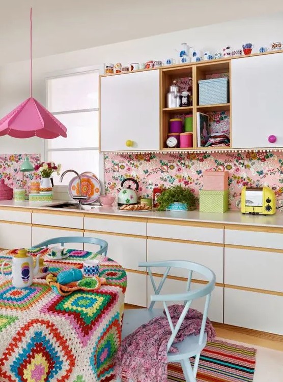 a bright retro kitchen with white flat panel cabinets, a bright pink wallpaper backsplash, a bright pink pendant lamp and pastel blue dining furniture