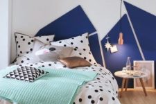 a catchy bedroom with a navy and white geometric decoration on the wall, a bed with polka dot bedding and a copper pendant lamp