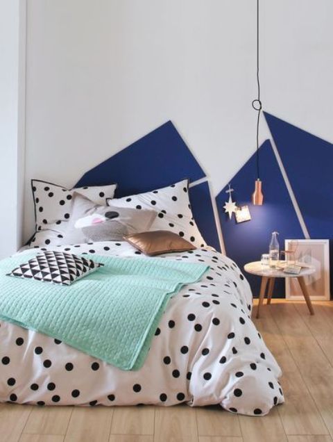 a catchy bedroom with a navy and white geometric decoration on the wall, a bed with polka dot bedding and a copper pendant lamp