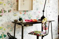 a catchy home office with a bright floral wall, a black desk and a floral chair, a black table lamp and some decor