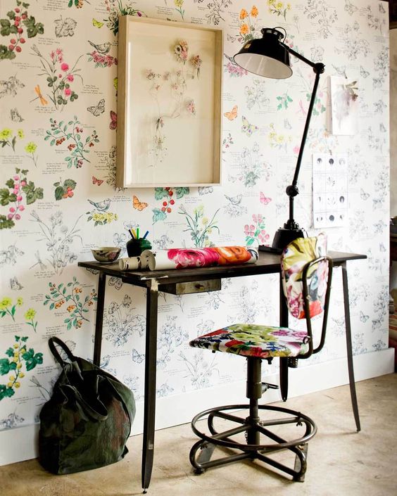 a catchy home office with a bright floral wall, a black desk and a floral chair, a black table lamp and some decor