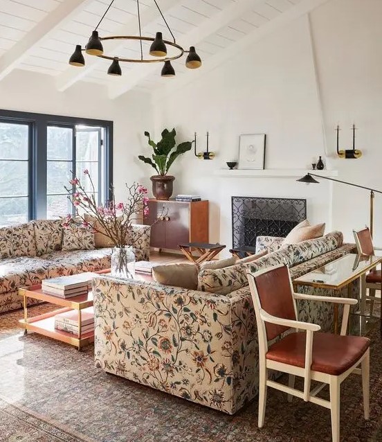 a catchy living room with a fireplace, floral sofas, a coffee table and a console table, black lamps and a chandelier