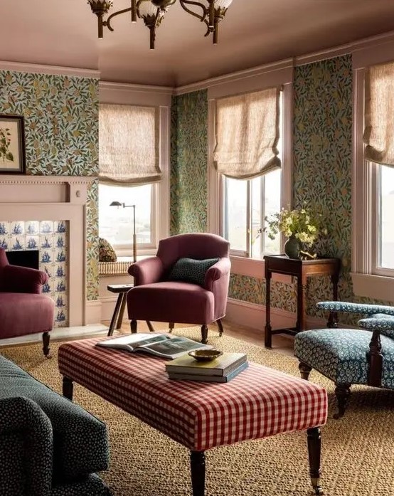 a catchy vintage living room with green floral wallpaper, a green sofa, burgundy chairs and a blue one, a plaid ottoman and a printed rug