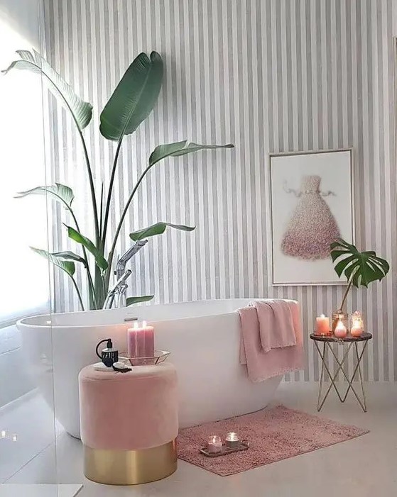 a charming girlish bathroom with a striped grey and white wall, a pink ottoman, a refined table and pink textiles