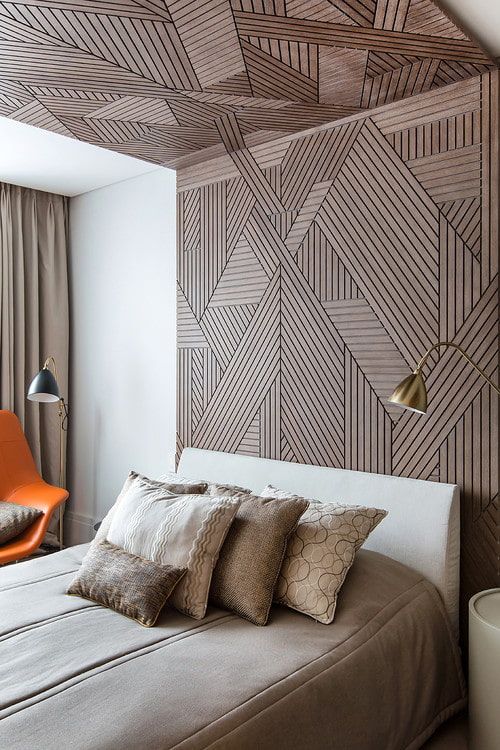 a chic bedroom with a beautiful wooden accent wall that goes up to the ceiling, a neutral bed with taupe bedding, an orange chair