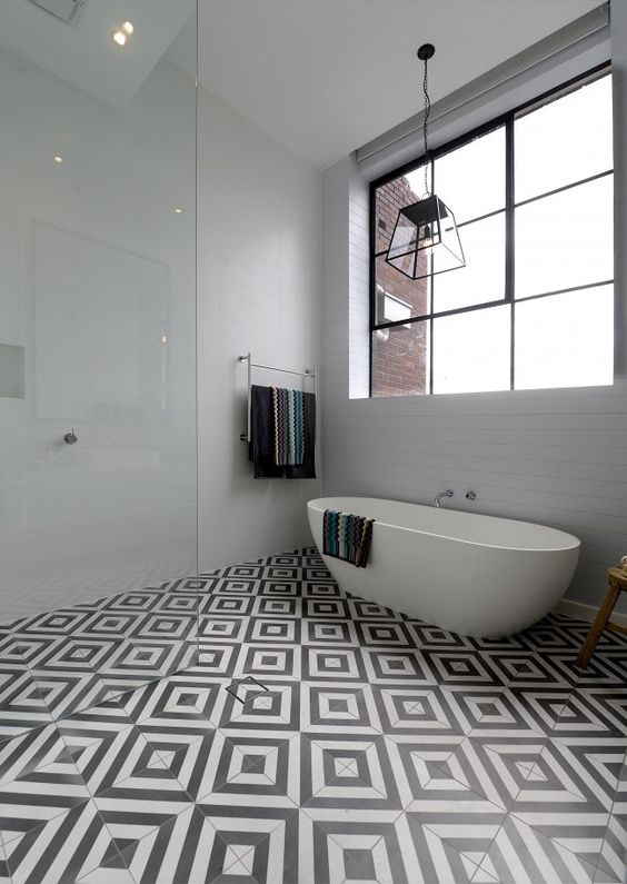 a chic contemporary bathroom with a black and white tile floor, a pendant lamp, an oval tub and printed textiles