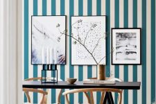 a chic dining room with a blue and white striped wall, a gallery wall, a black table and refined wooden chairs