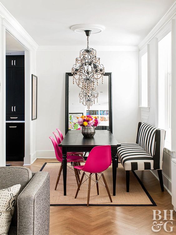 a chic dining space with a statement mirror, a black table, fuchsia chairs, a striped bench and a chic and bold chandelier